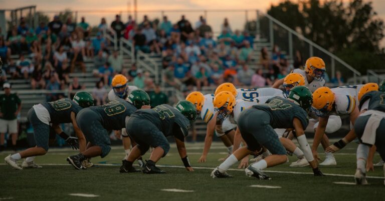 Teams face off in an intense high school football game as the sun sets, adding drama to the scene.